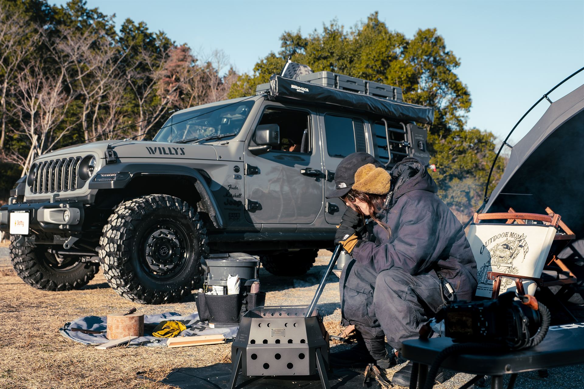 Jeep Wranglerのそばで焚き火を楽しむYOHEIさん